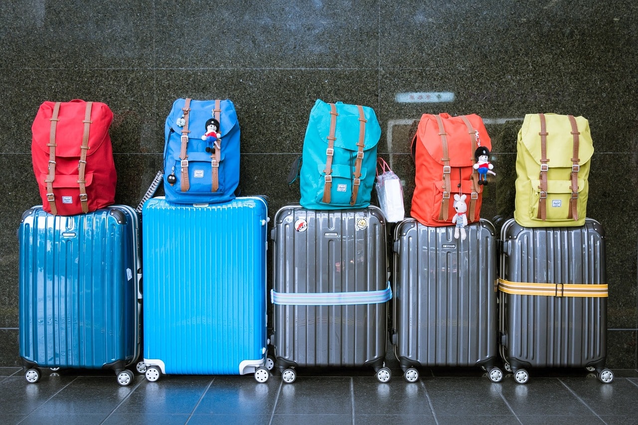 Plusieurs valises côte à côte sur lesquelles sont empilées des sacs à dos de toutes les couleurs