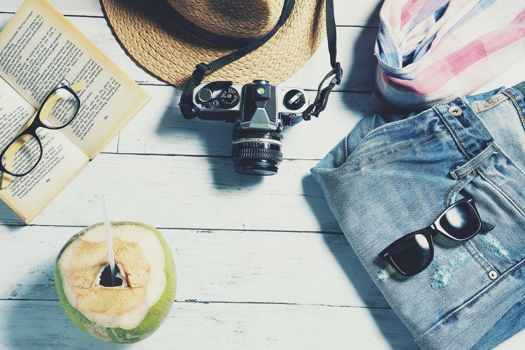 noix de coco, livre, appareil photo, chapeau, lunettes de soleil et short posés sur des planches